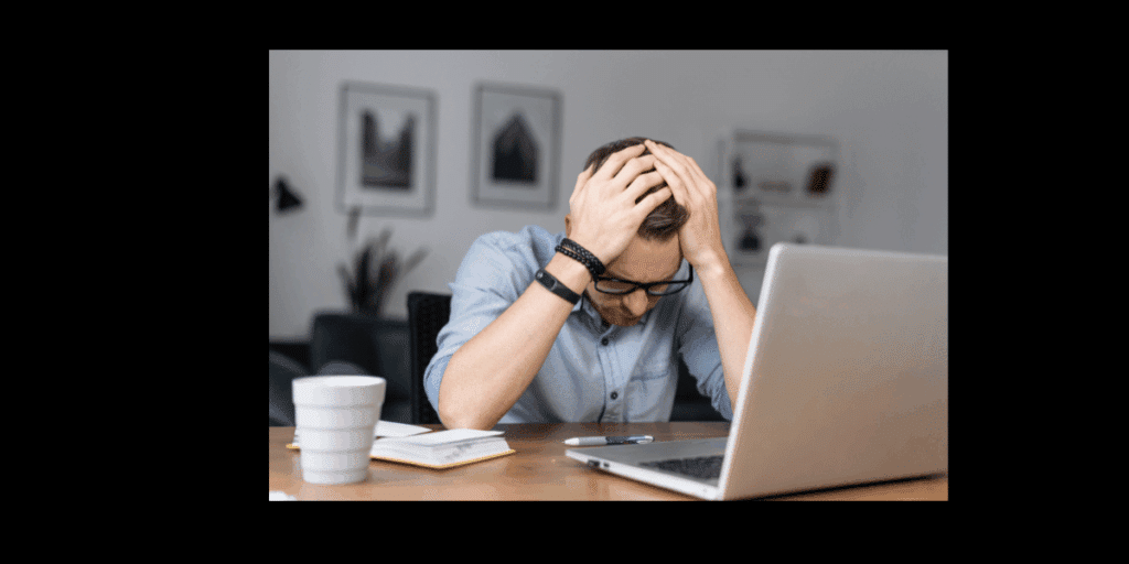 A tired, stressed man holding his head at a desk in front of a laptop, representing frustration with complex learning